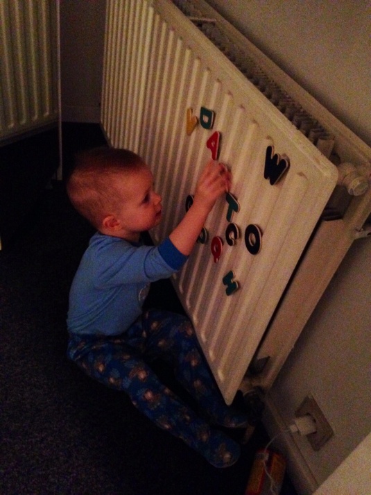Playing in the hotel room after a long day of sight-seeing, and excited to discover that his letter magnets stick to the radiator!  (Don't worry, the radiator isn't on...)
